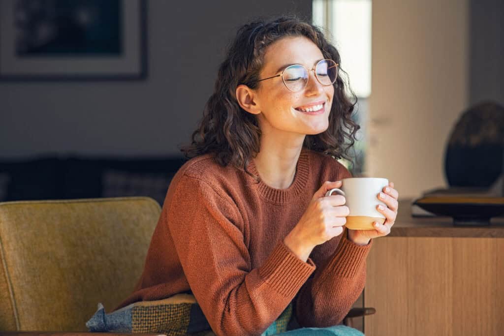 Vrouw geniet ontspannen met een kopje koffie in een stille, sfeervolle woonkamer met warme kleuren