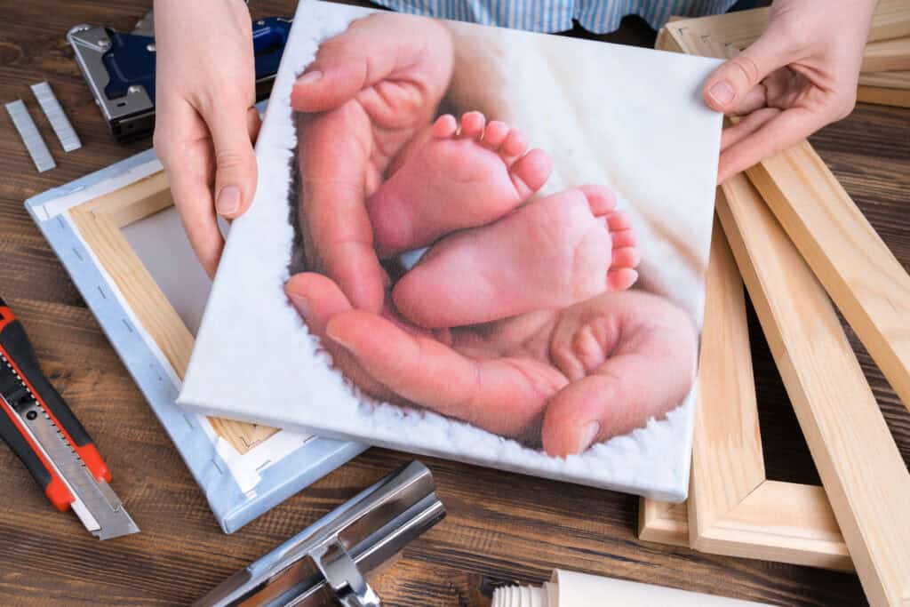 Canvasdoek met foto van babyvoetjes in handen, omringd door materialen voor montage – symbool voor persoonlijke wanddecoratie