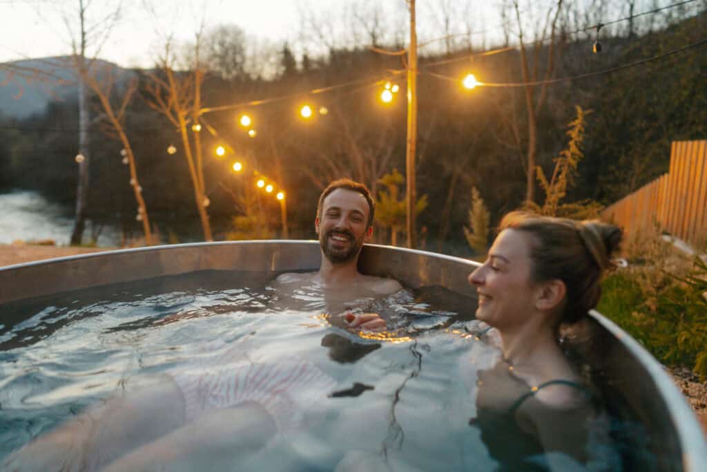 Stel genietend in een hottub in de tuin tijdens zonsondergang, omringd door sfeerverlichting.