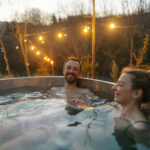 Stel genietend in een hottub in de tuin tijdens zonsondergang, omringd door sfeerverlichting.