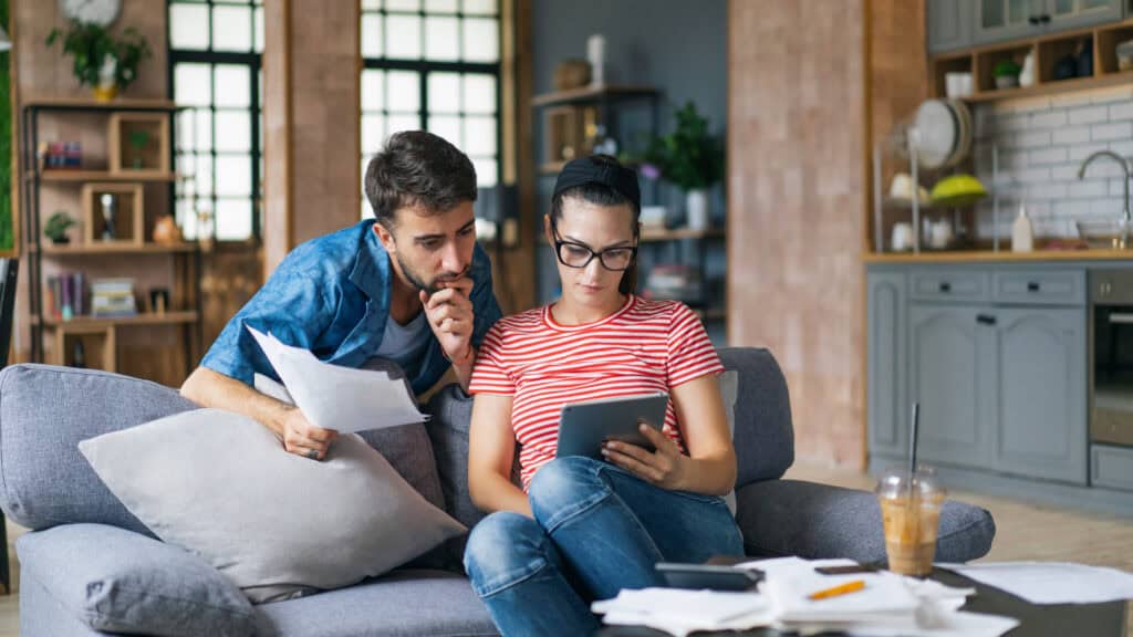 Jonge starters bekijken samen hypotheekopties op een tablet, met papieren op tafel in een huiselijke setting