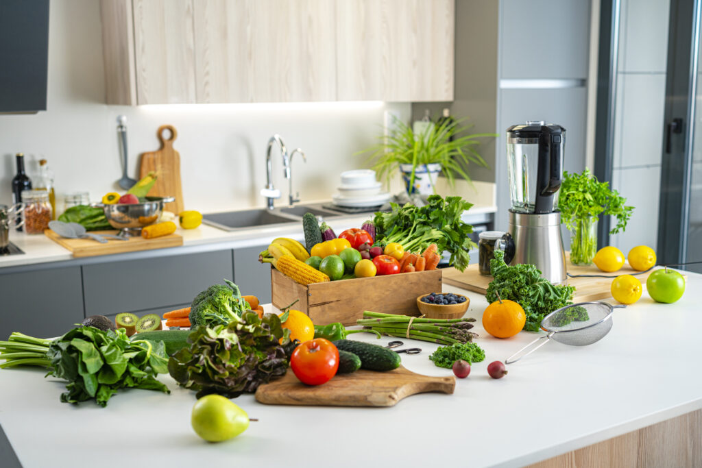 Keukentafel vol verse groenten en fruit in een moderne keuken, met blender en houten elementen
