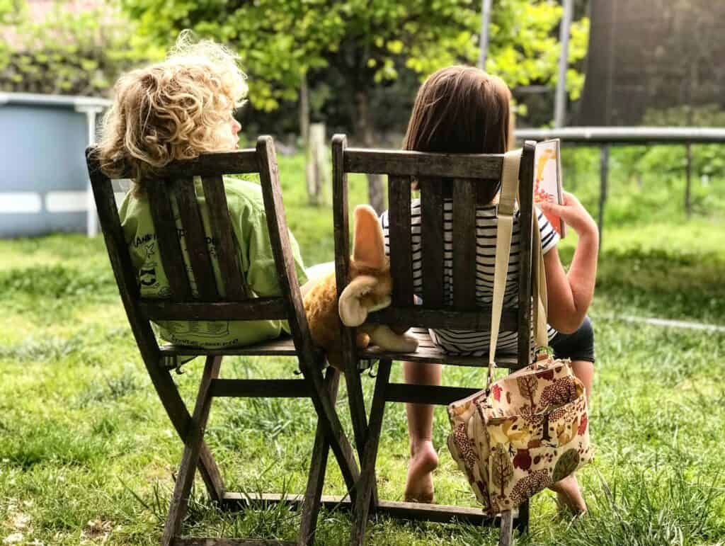 Twee kinderen ontspannen op houten tuinstoelen in het gras tijdens een zonnige middag in de tuin