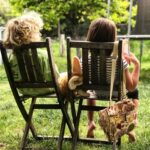 Twee kinderen ontspannen op houten tuinstoelen in het gras tijdens een zonnige middag in de tuin