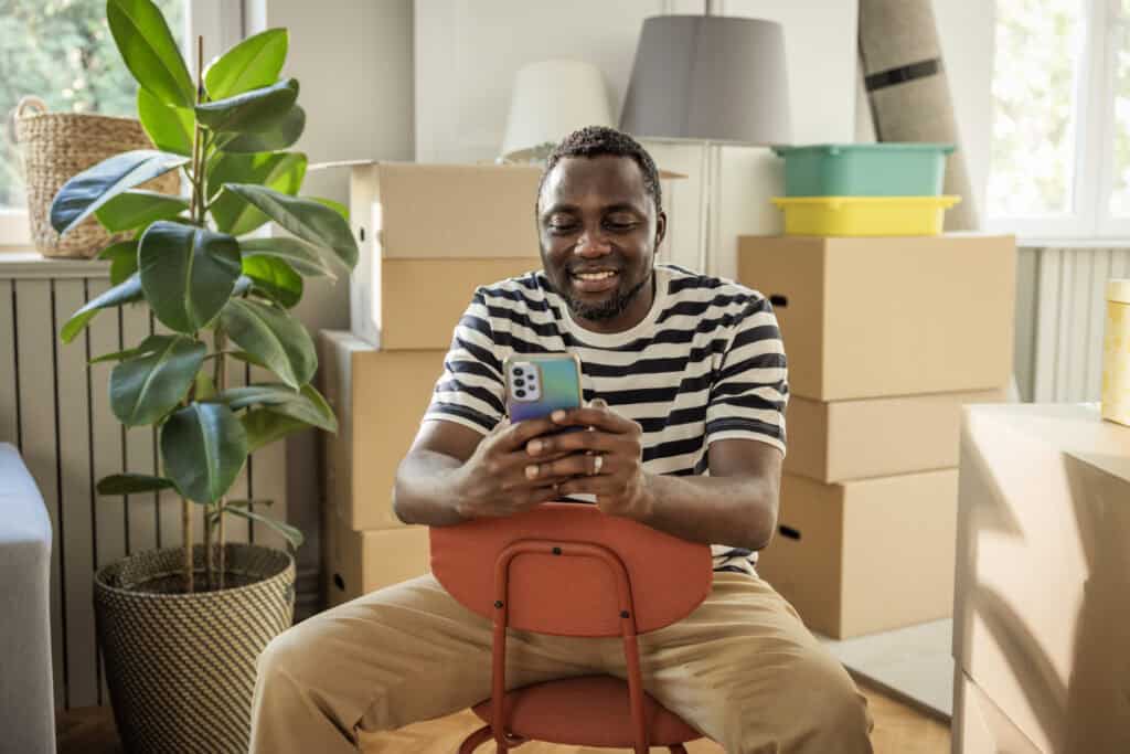 Man tussen verhuisdozen die op zijn telefoon iets regelt na een recente verhuizing