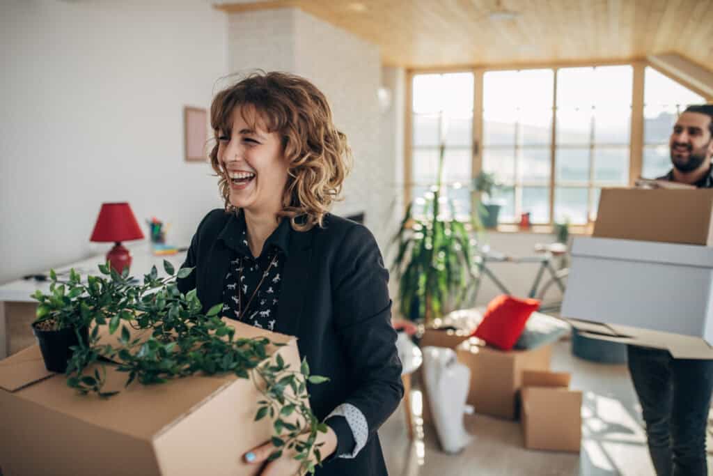 Lachende vrouw tilt een verhuisdoos met kamerplanten tijdens verhuizing