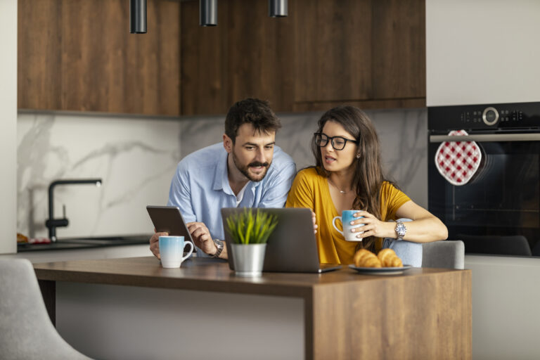 Jong stel aan keukentafel bekijkt laptop en tablet om zelf hun hypotheek te regelen