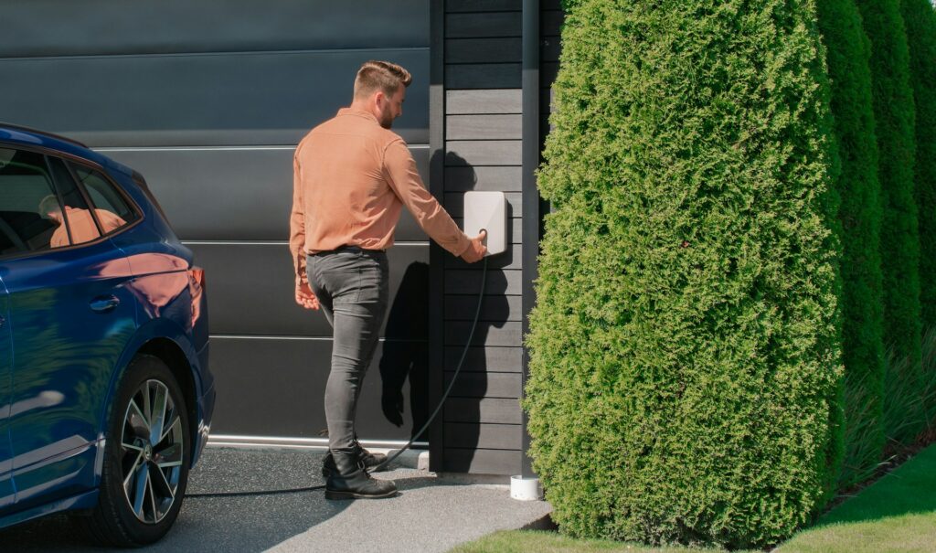 Man sluit elektrische auto aan op laadpaal bij woning