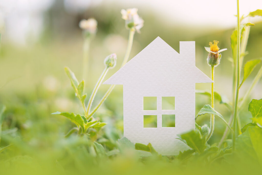 Wit papieren huisje tussen groene planten symboliseert duurzaam en natuurinclusief bouwen