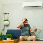 Man kijkt gefrustreerd naar energierekening onder airco in zijn woonkamer