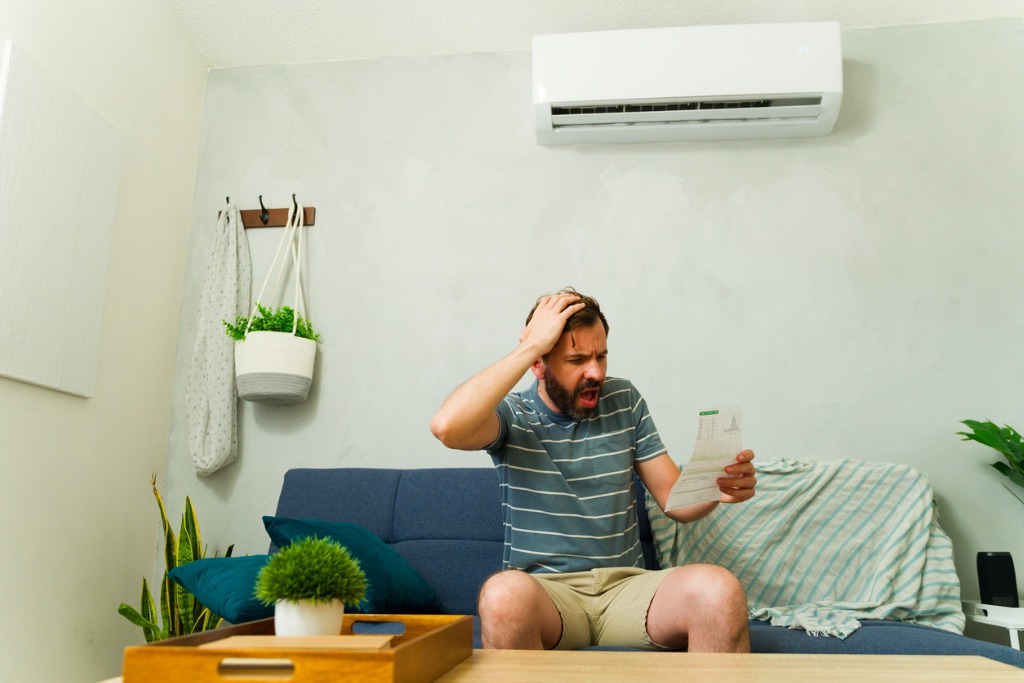 Man kijkt gefrustreerd naar energierekening onder airco in zijn woonkamer