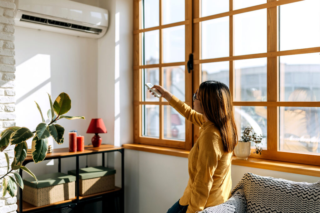 Vrouw bedient airconditioner met afstandsbediening in een zonnige, moderne woonkamer