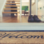 Welcome deurmat bij een moderne hal met schoenen, houten vloer en open trap