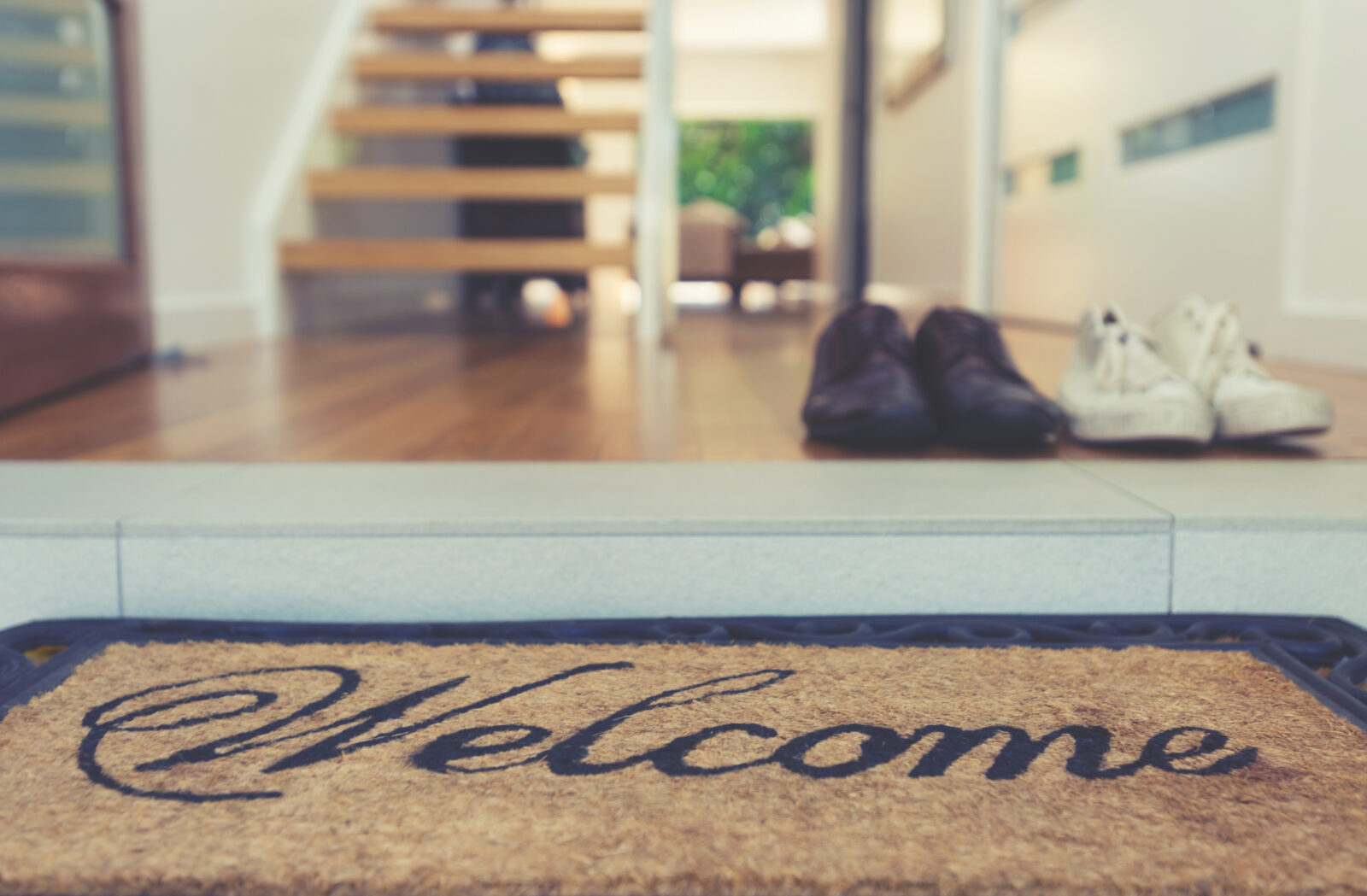 Welcome deurmat bij een moderne hal met schoenen, houten vloer en open trap