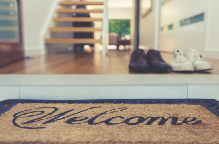 Welcome deurmat bij een moderne hal met schoenen, houten vloer en open trap