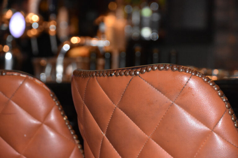 Close-up van twee cognackleurige leren eetkamerstoelen met ruitstiksels in een warme setting