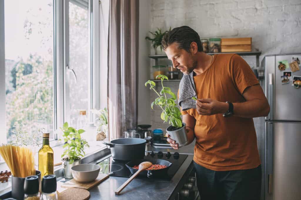Man voegt verse basilicum toe tijdens het koken op een inductiekookplaat in een lichte, moderne keuken