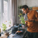 Man voegt verse basilicum toe tijdens het koken op een inductiekookplaat in een lichte, moderne keuken