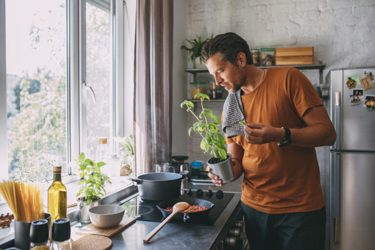 Man voegt verse basilicum toe tijdens het koken op een inductiekookplaat in een lichte, moderne keuken