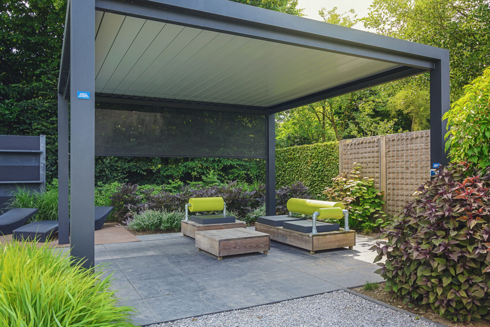 Aluminium overkapping met verstelbaar dak in een groene tuin, voorzien van moderne loungemeubels