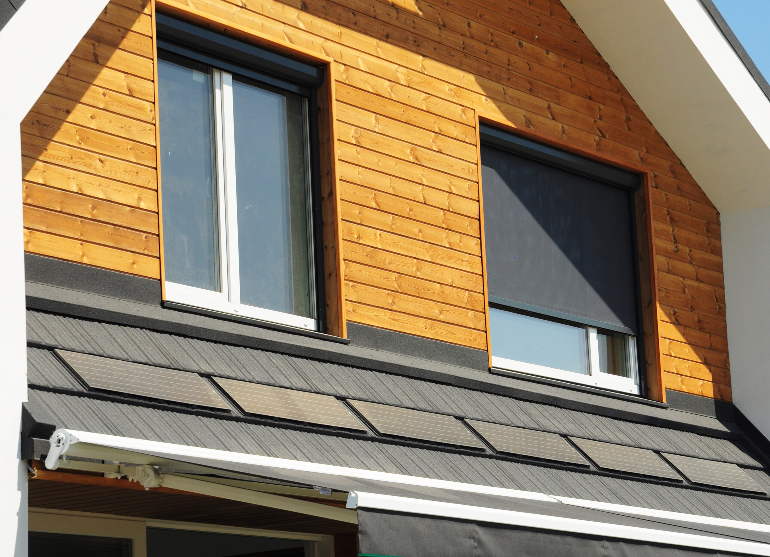 Woning met houten gevel en gesloten screen als zonwering op een zonnige dag
