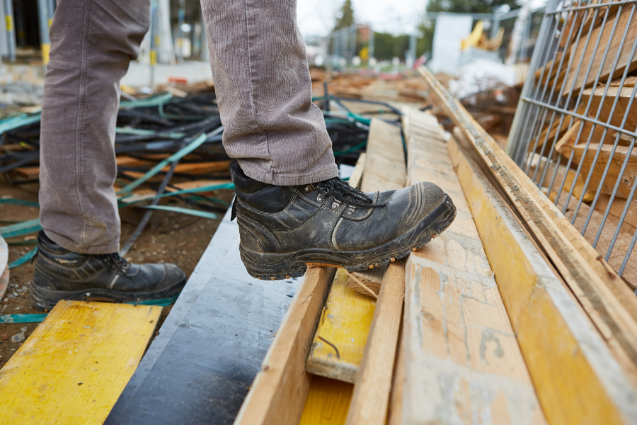 Close-up van veiligheidsschoenen op losse planken en rommelige ondergrond tijdens kluswerk