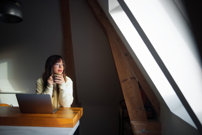 Vrouw met kop koffie geniet van het daglicht in een zolderkamer met dakkapel