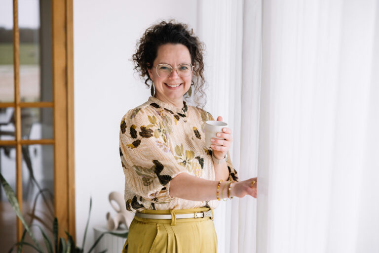 Interieurontwerper Els van Maren van Studio Els kijkt glimlachend uit het raam met een kopje koffie in haar hand