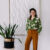 Els van Maren poseert lachend in haar studio naast een groene plant en een kunstwerk van wit textiel