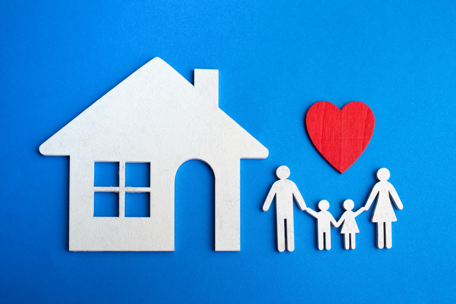 Papieren gezin met rood hart en huisvorm tegen een blauwe achtergrond als symbool voor woonveiligheid en liefdevol thuis.