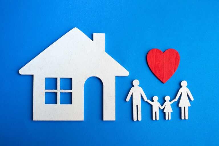 Papieren gezin met rood hart en huisvorm tegen een blauwe achtergrond als symbool voor woonveiligheid en liefdevol thuis.