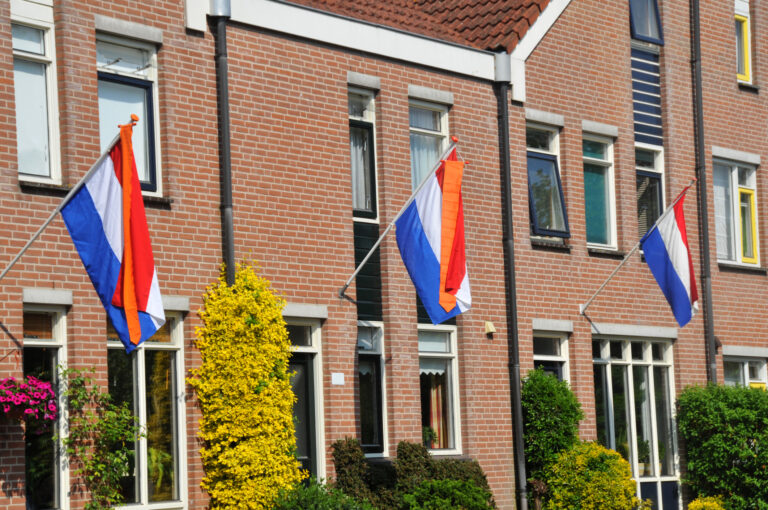 Drie Nederlandse vlaggen met oranje wimpel aan de gevel van rijtjeshuizen