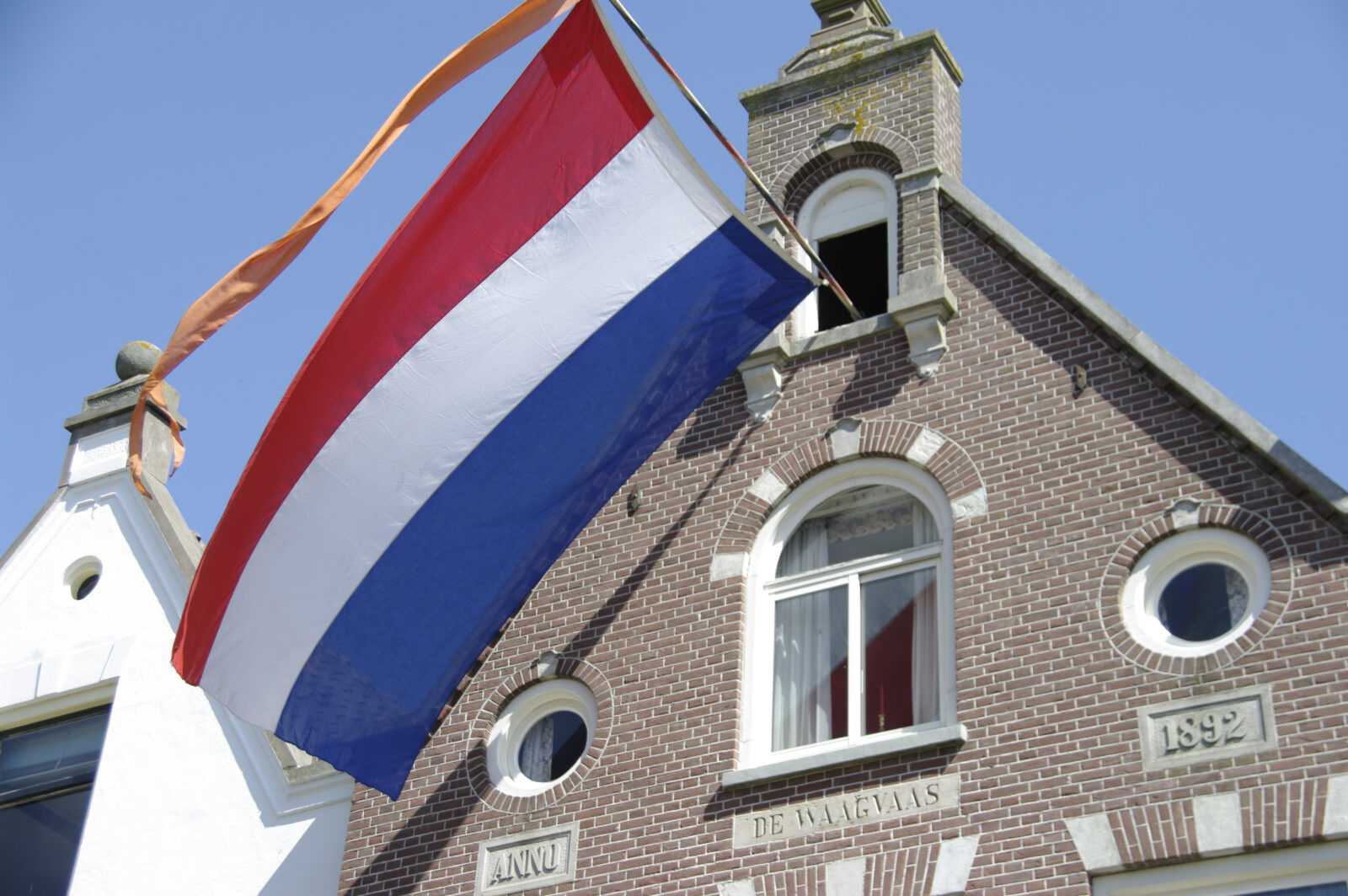 Wapperende Nederlandse vlag met oranje wimpel aan een oud gebouw met gevelsteen 'Anno 1892'