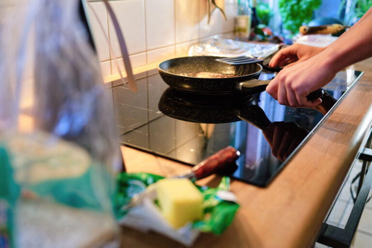 Handen die koken op een moderne inductiekookplaat met een pan en verse ingrediënten op het aanrecht.