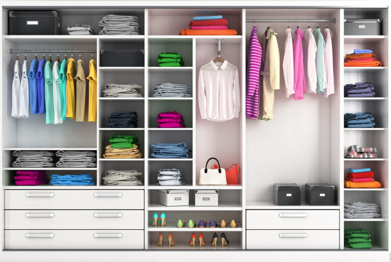 Georganiseerde moderne kledingkast met op kleur gesorteerde kleding, schoenen en opbergdozen in een wit kastensysteem