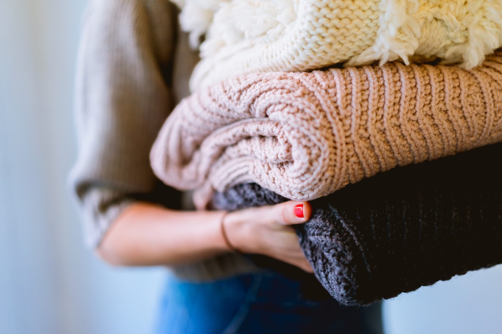 Vrouw met opgevouwen gebreide truien in natuurlijke tinten zoals beige, crème en antraciet