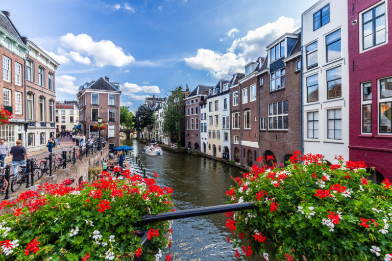 Zomerse gracht in Utrecht met kleurrijke bloemen, fietsers en voorbijvarende bootjes