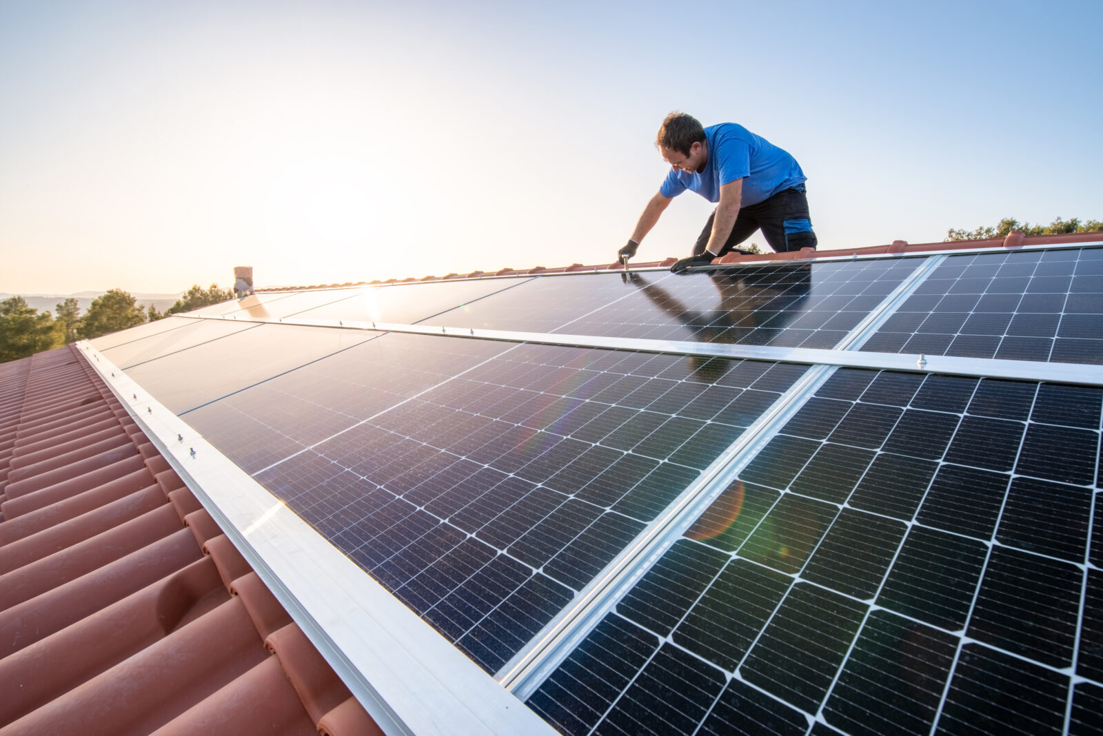 Monteur plaatst zonnepanelen op een dak bij zonsondergang