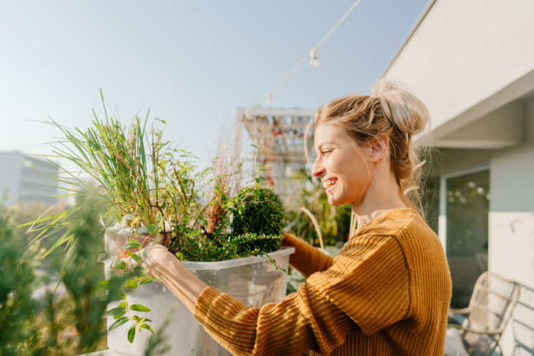 Vrouw verzorgt planten op een zonnig balkon als onderdeel van duurzaam en slim tuinieren