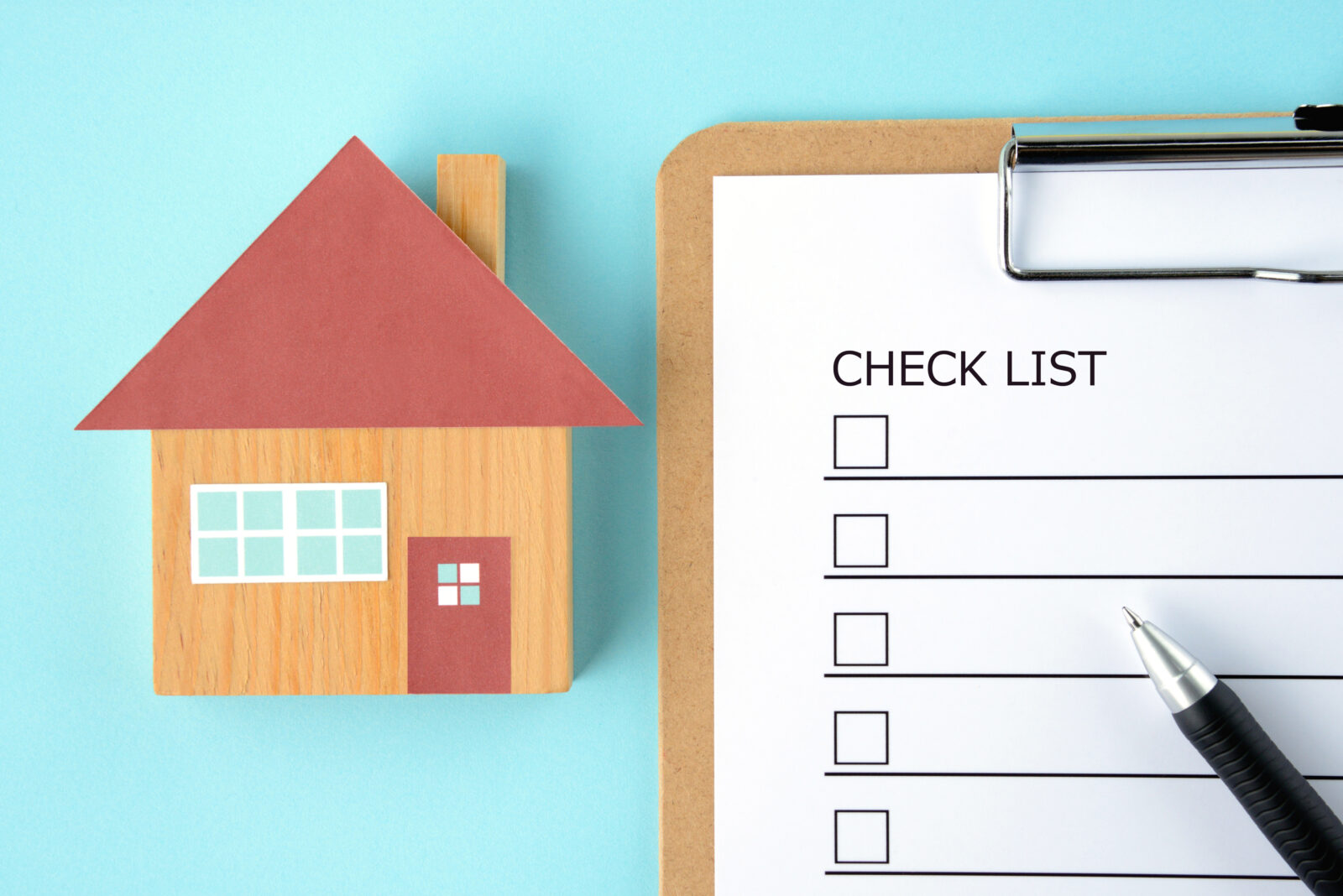 Checklist voor een veilig huis met houten huismodel en pen.