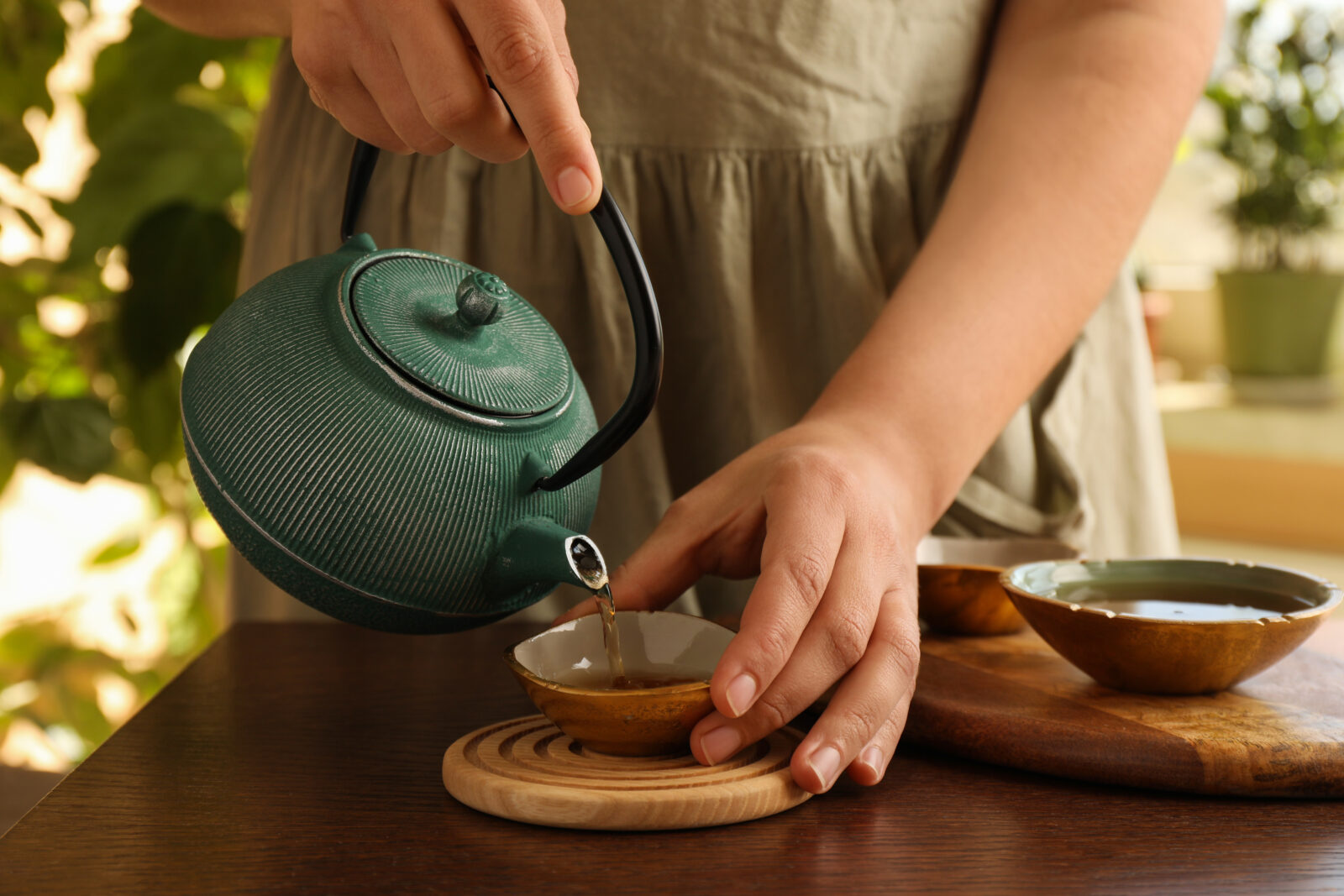 Handen schenken thee uit een gietijzeren theepot in Japandi-stijl op houten tafel