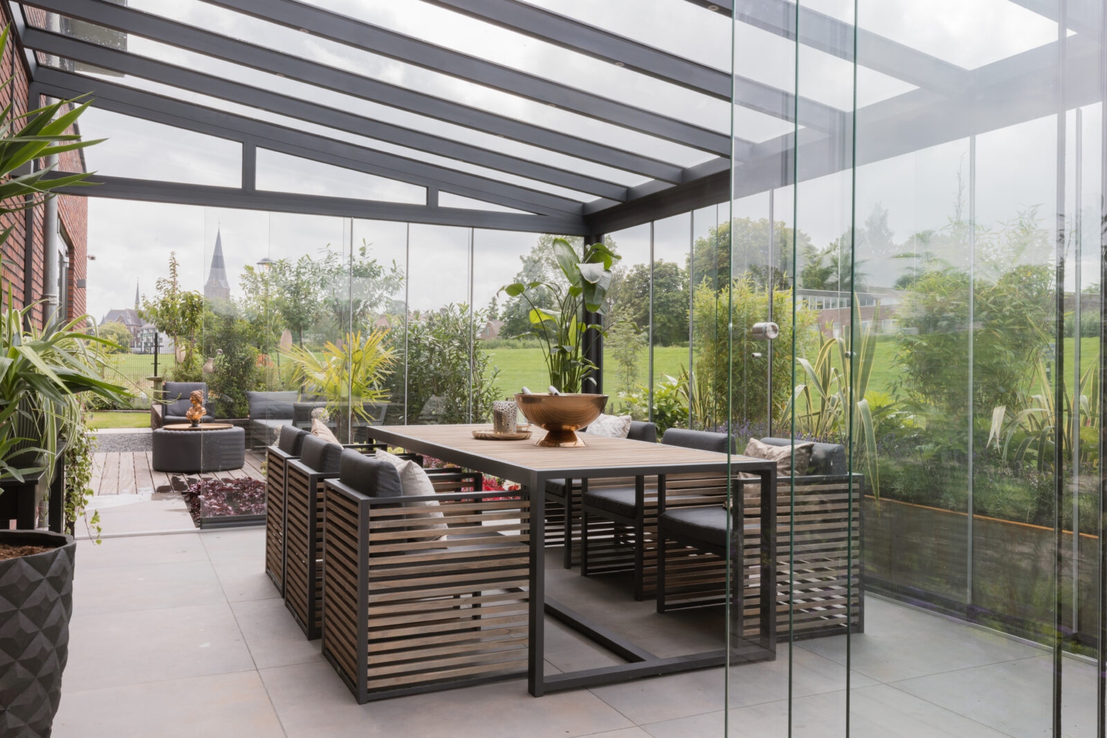 Stijlvolle veranda met glazen wanden en moderne eettafel in een groene tuin