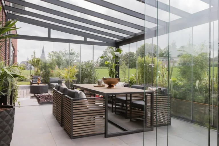 Stijlvolle veranda met glazen wanden en moderne eettafel in een groene tuin
