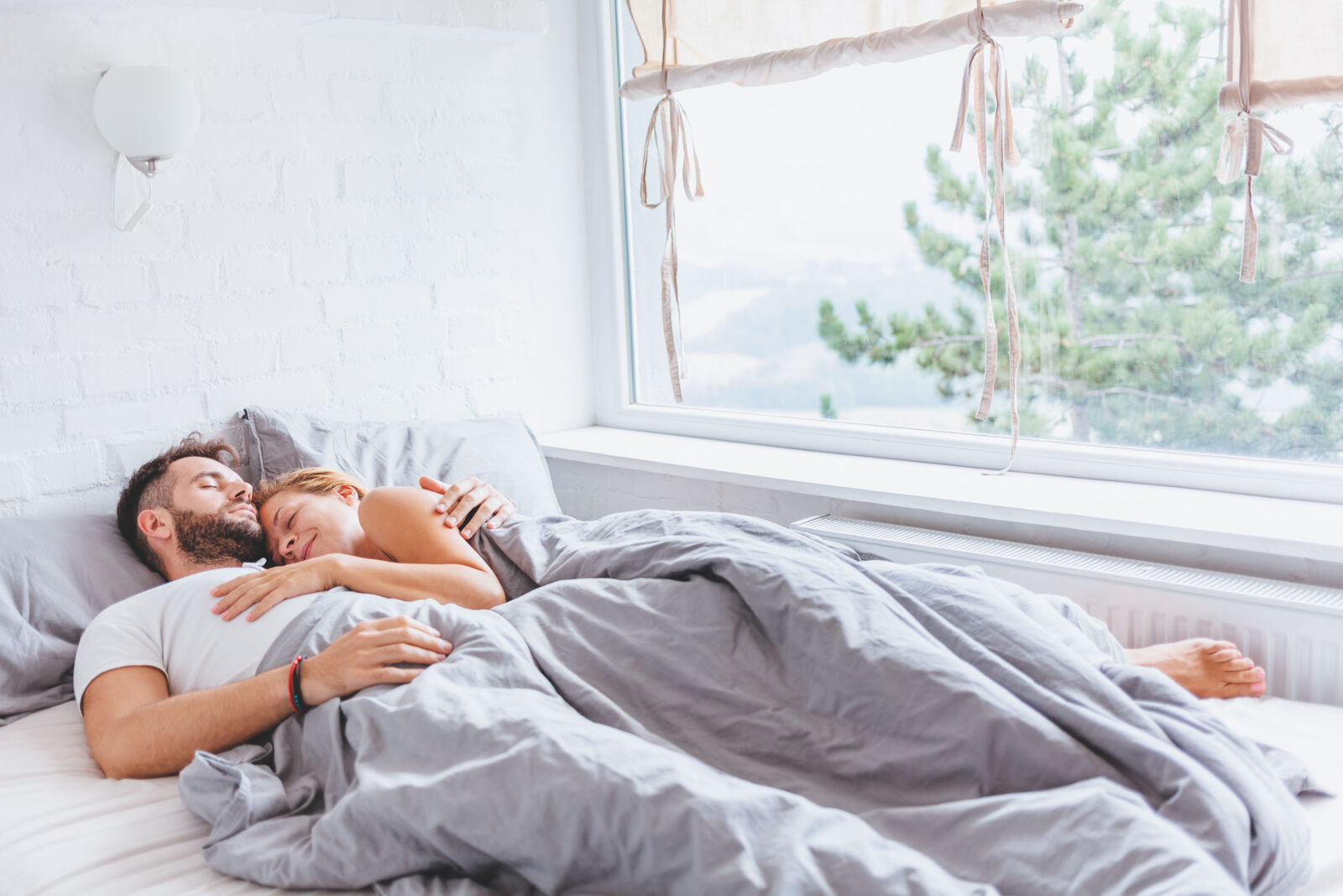 Koppel slaapt ontspannen in een frisse slaapkamer met open raam en licht beddengoed