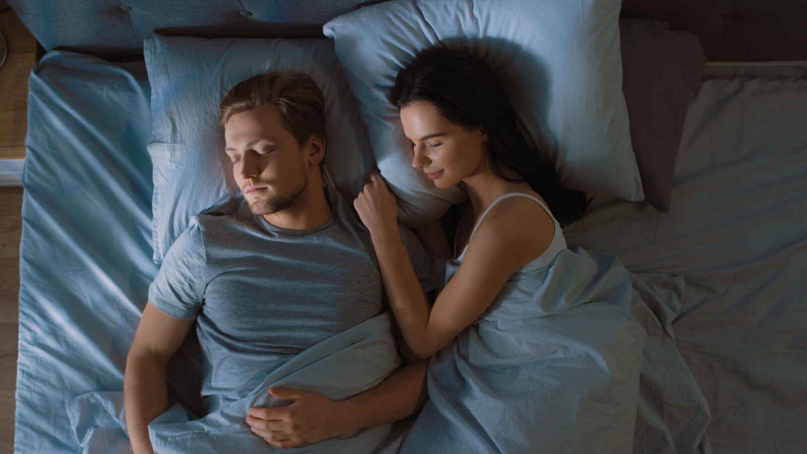 Stel ligt ’s nachts in bed onder blauw licht, symbool voor onrustig slapen tijdens warme nachten