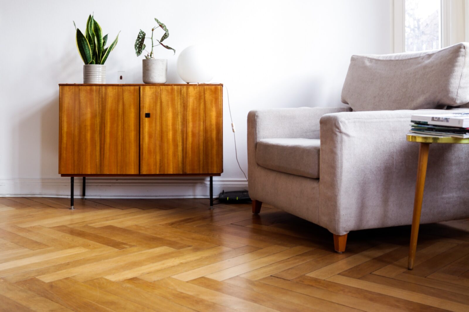 Klassieke houten visgraatvloer in een woonkamer met een vintage dressoir en een beige fauteuil