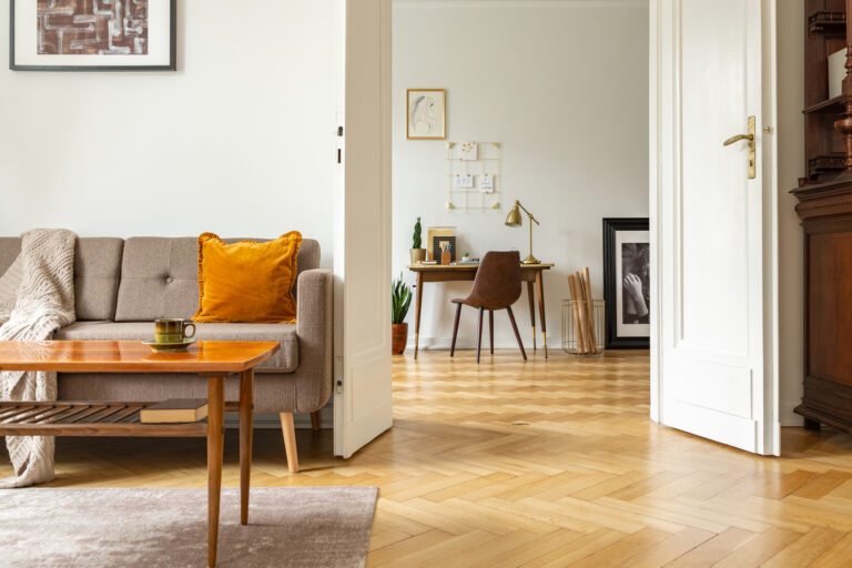 Licht eiken visgraatvloer in een gezellige woonkamer met vintage bank en doorkijk naar een werkhoek met bureau en planten