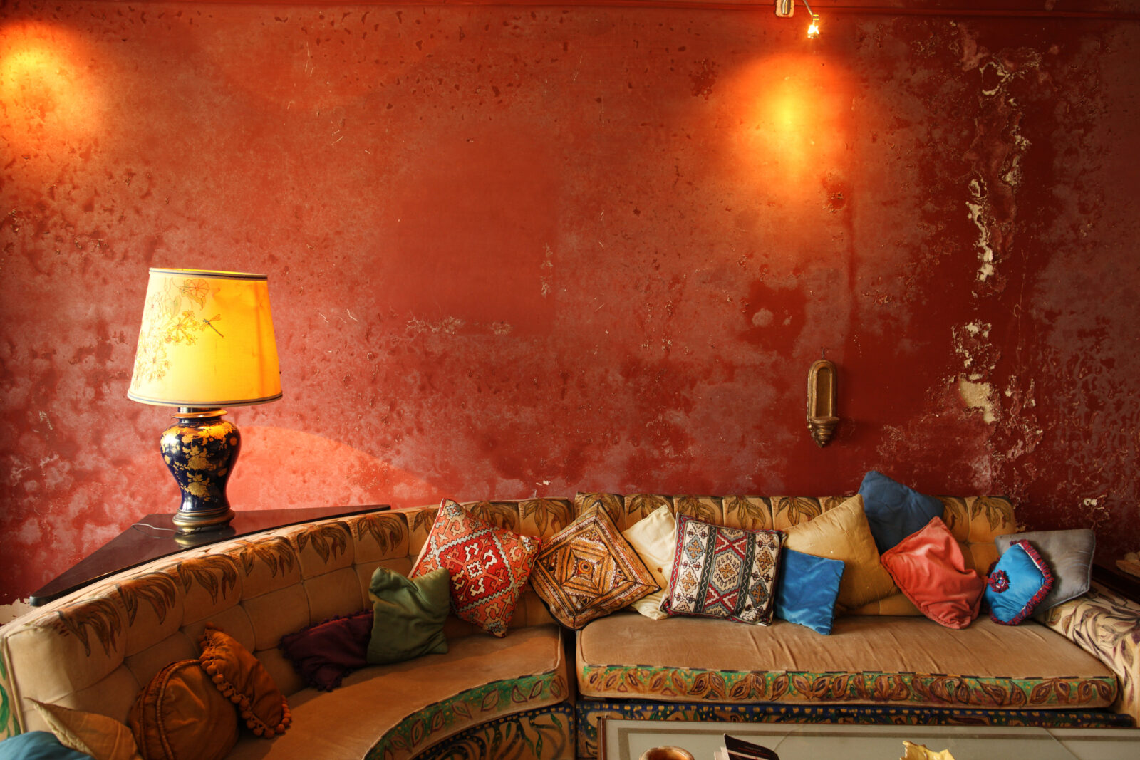 Warme woonkamer met rode muur, lamp en kleurrijke kussens, passend bij Intriguing Decor.