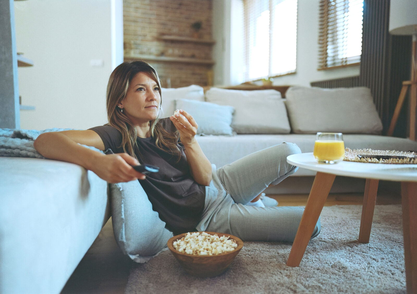 Vrouw zit ontspannen op de grond met popcorn en kijkt televisie in een moderne woonkamer