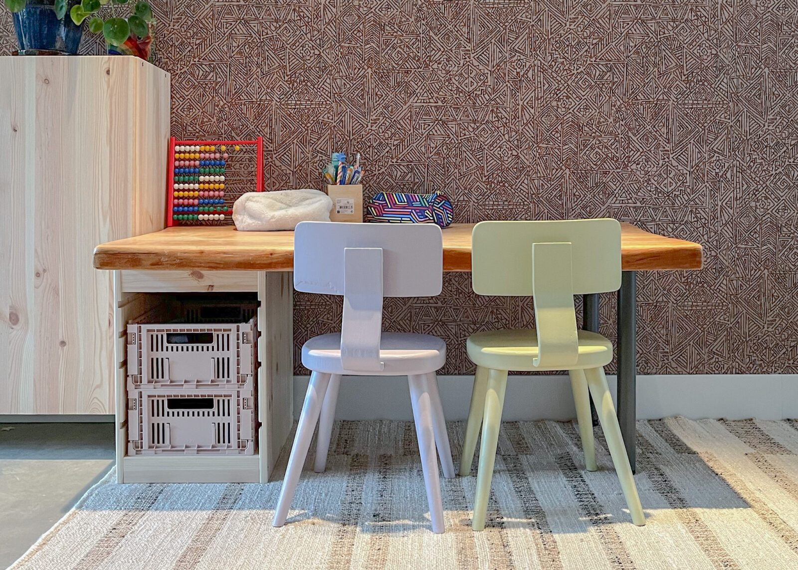 Slim ingerichte speelhoek met houten bureau, twee kinderstoeltjes en handige opbergbakken – ontwerp van Bente Metselaar
